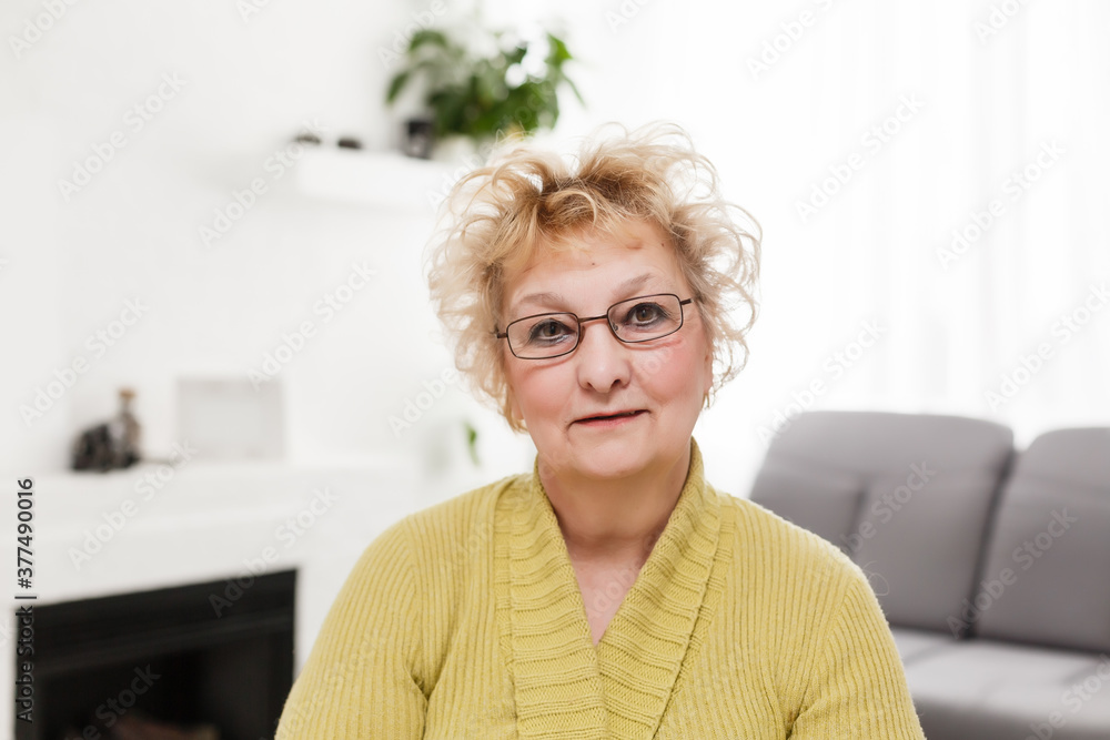 Attractive elderly woman sitting on couch at home, looking at camera, makes video call, communication distantly, modern wireless technologies concept Attractive elderly woman sitting on couch at home, looking at camera, makes video call, communication distantly, modern wireless technologies concept