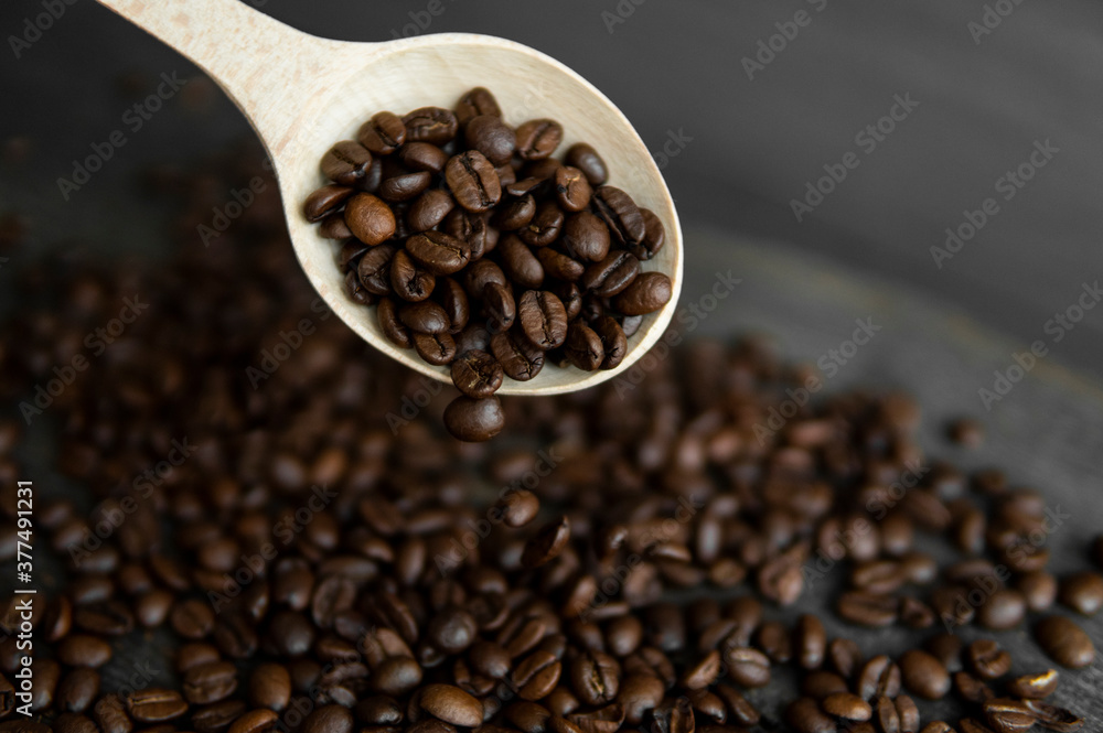 Fresh roasted arabica coffee beans falling from a oaken spoon on a wooden table.