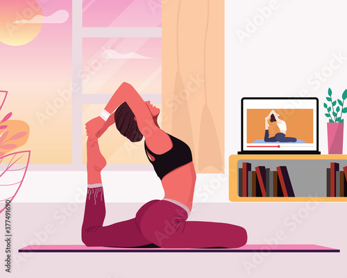 Woman doing yoga on a mat following online classes with laptop at home