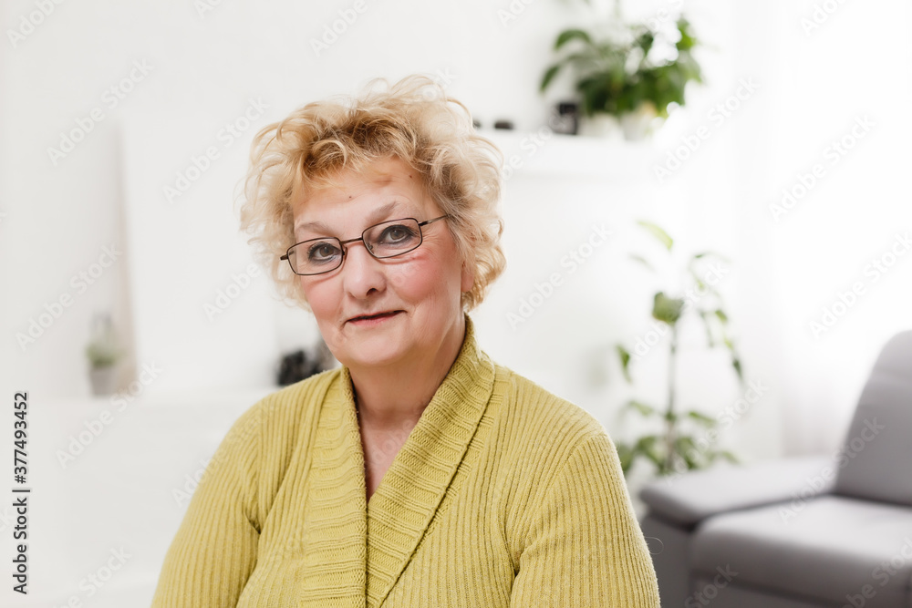 Smiling middle aged mature grey haired woman looking at camera, happy old lady in glasses posing at home indoor, positive single senior retired female sitting on sofa in living room headshot portrait Smiling middle aged mature grey haired woman looking at camera, happy old lady in glasses posing at home indoor, positive single senior retired female sitting on sofa in living room headshot portrait