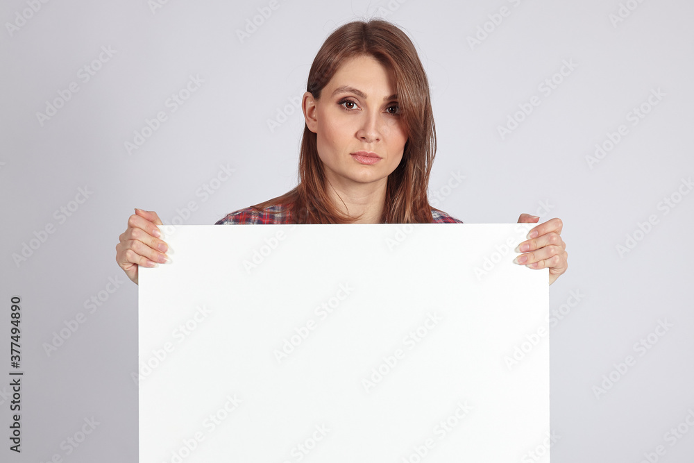 Young attractive woman with dark brown hair and eyes holds empty white board or banner with great copy space for any text or slogan. Serious look, confident face expression, concernity concept. Young attractive woman with dark brown hair and eyes holds empty white board or banner with great copy space for any text or slogan. Serious look, confident face expression, concernity concept.