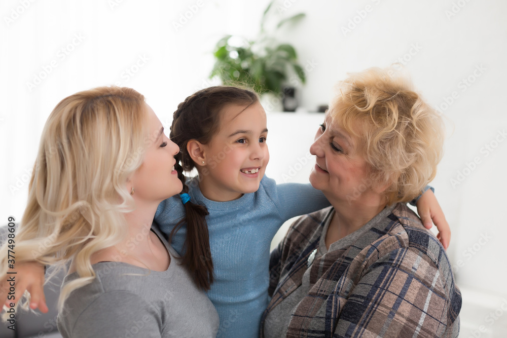 Three generations of women. Beautiful woman and teenage girl are kissing their granny while sitting on couch at home Three generations of women. Beautiful woman and teenage girl are kissing their granny while sitting on couch at home