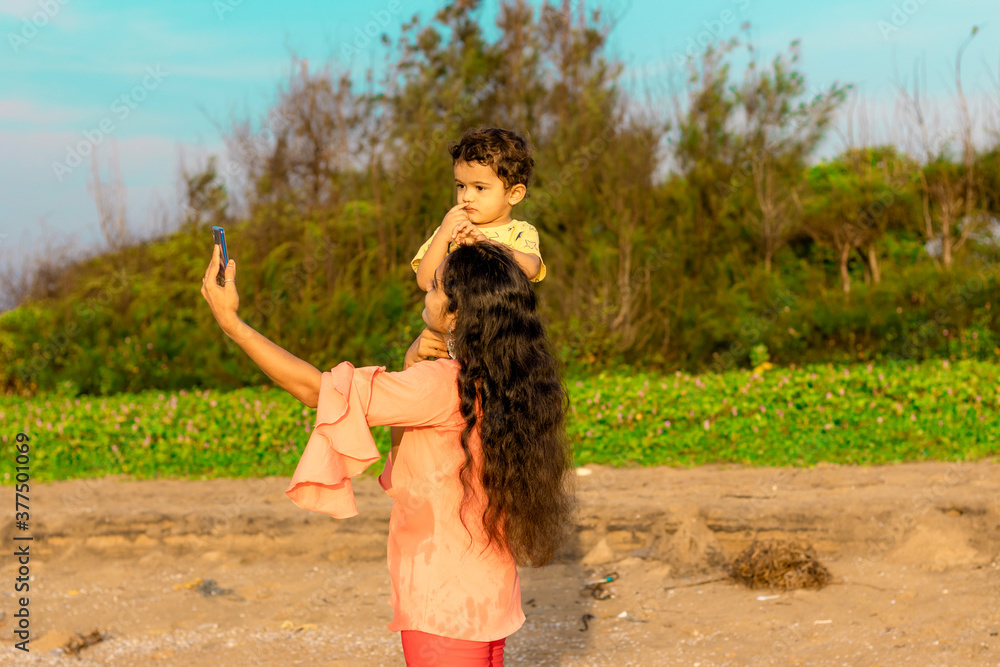 An Indian mother seated baby on her shoulder and took a selfie from a smart mobile, outdoor people