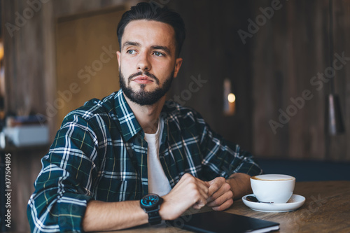 Serious man looking away while drinking coffee in cafe