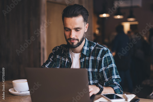 Focused young businessman with laptop in loft cafe during remote work