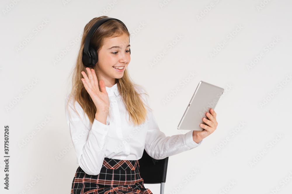 Cute smiling teen girl in school uniform with headphones and tablet in her hands isolated on the white background Cute smiling teen girl in school uniform with headphones and tablet in her hands isolated on the white background
