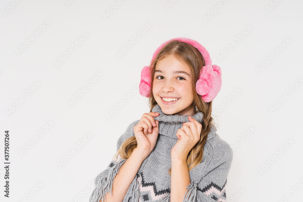 Cute smiling teenage girl in pink fur headphones and gray poncho looks up isolated on the white background Cute smiling teenage girl in pink fur headphones and gray poncho looks up isolated on the white background