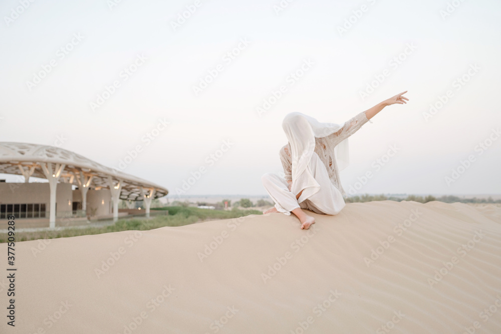 Woman sitting on the sand dune showing direction Woman sitting on the sand dune showing direction