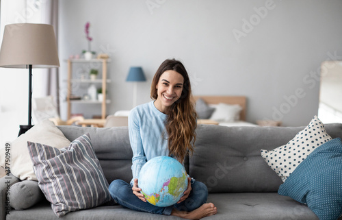 Young smiling girl holding a globe while sitting on the sofa at home.