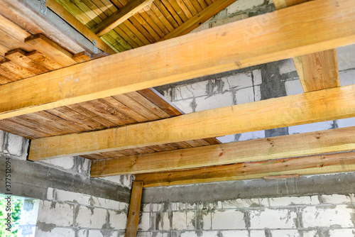 Wooden joists prepared for laying the attic floor of a newly built white brick house.