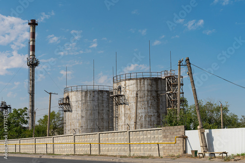 Industrial area in the city. Elevator tanks for grain storage. Big pipe. Fenced territory of the industrial zone. Blue sky and clouds over the industrial area