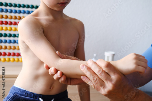 male doctor pediatrician  orthopedist examines a little patient  his hand  kid  boy sits on a chair in the office  the concept of health insurance  limb injury  examination  treatment