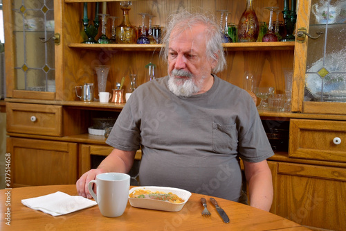 Depressold man, self isolating due to COVID-19, eating a TV dinner alone..Lonely old man eating by himself.