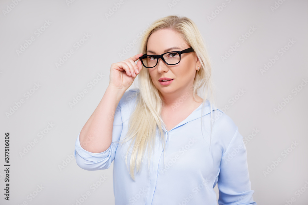 beautiful plus size blonde business woman or teacher in eyeglasses posing over gray beautiful plus size blonde business woman or teacher in eyeglasses posing over gray