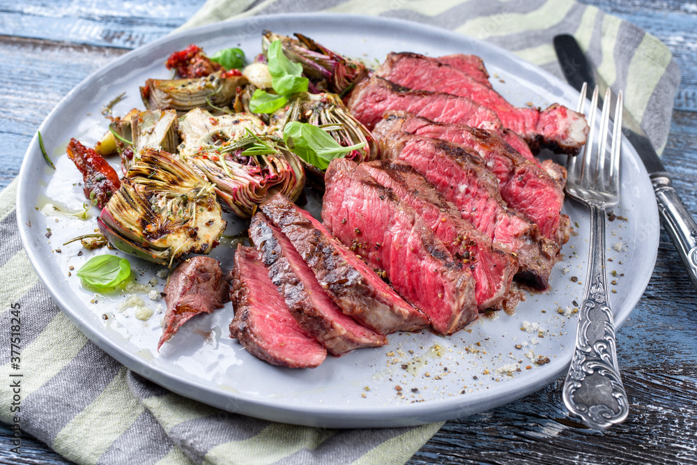 Traditional barbecue angus entrecote beef steak with artichoke hearts and herbs offered as close-up on a Modern Nordic design plate Traditional barbecue angus entrecote beef steak with artichoke hearts and herbs offered as close-up on a Modern Nordic design plate