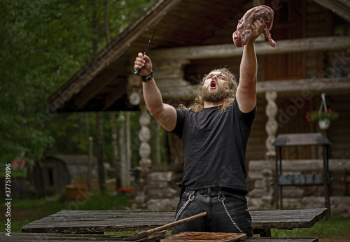 Brutal long hair man prepare meat near forest house