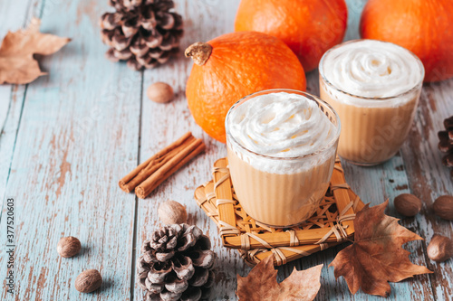 Pumpkin pie smoothie on worn wooden table with cedar cones and dry leaves. Autumn still life with pumpkin smoothie decorated with whipped cream closeup