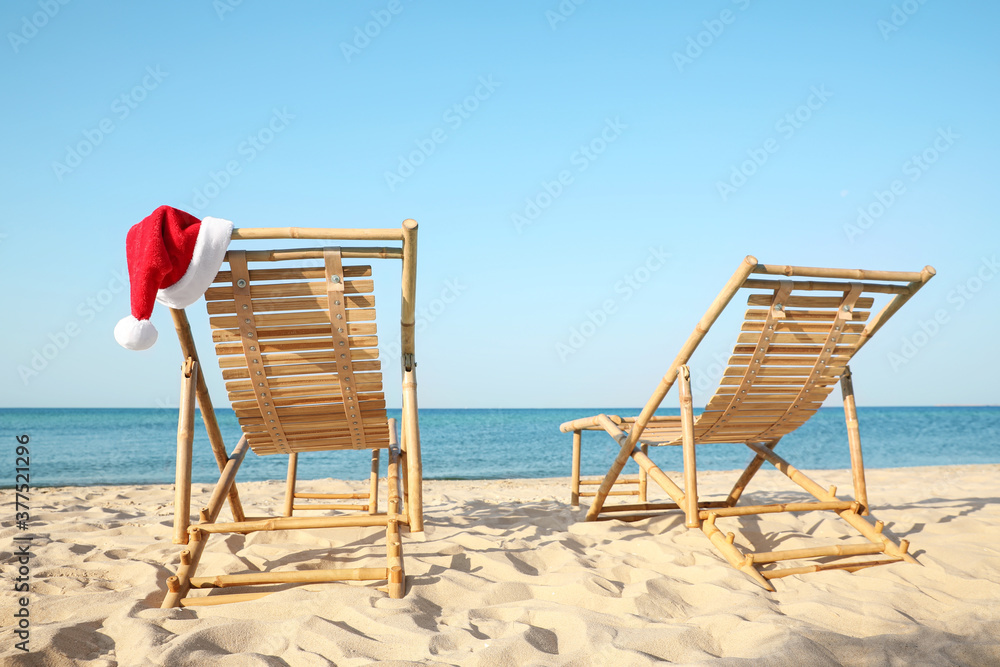 Sun loungers and Santa's hat on beach. Christmas vacation