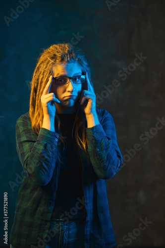 Sad girl in colorful neon lighting on dark background.