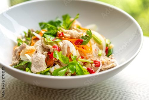 Thai food, spicy salad of cleared noodles or Yum Woon Sen in Thailand language. Close up food in white bowl on table, natural light.