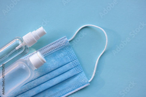 Disposable medical face mask and hand sanitizer bottles on blue background with copy space. Pandemic protective kit. 