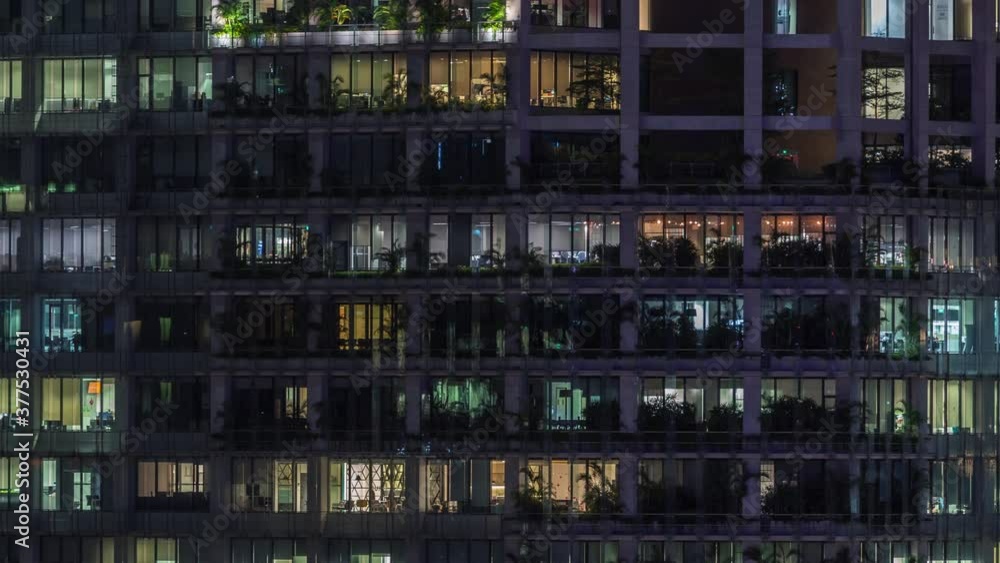 Modern office building with big windows at night timelapse close up view, in windows glowing light shines and some people inside, Singapore Modern office building with big windows at night timelapse close up view, in windows glowing light shines and some people inside, Singapore