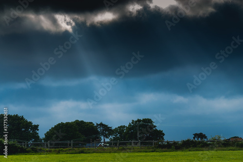 Image showing a bright green field with streaks of light coming down from a dark and moody sky. No People
