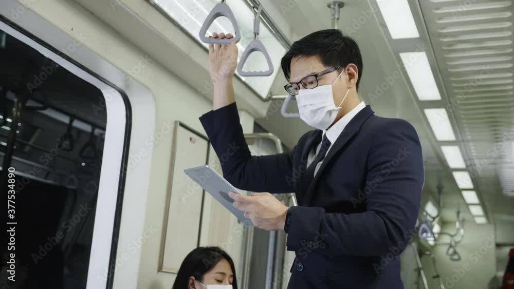 Asian business man wear face mask and read online news about invest in a tablet. Travel on modern subway transport. Wearing a mask is a modern lifestyle. Concept New Normal Asian business man wear face mask and read online news about invest in a tablet. Travel on modern subway transport. Wearing a mask is a modern lifestyle. Concept New Normal