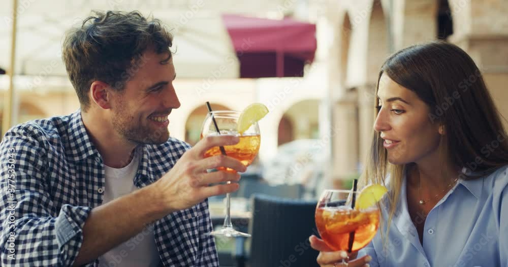 An young carefree romantic happy couple in love is drinking and cheating with cool alcohol cocktails while enjoying a happy hour time together in city center bar on a weekend in a sunny day.
