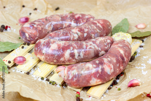 Fresh raw uncooked homemade pork sausages with garlic and spices on light wooden background in the kitchen.