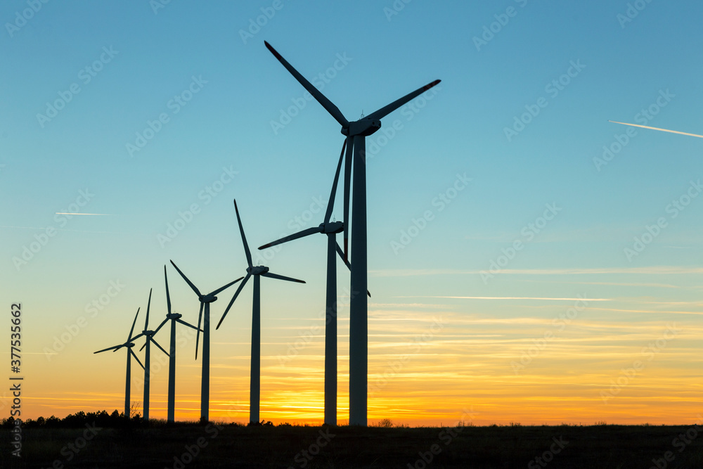 Wind Turbines at Dusk. Landscape sunset with windmills. Renewal source of electricity. Wind turbines field new technology for clean energy on mountain, sunset view with colorful twilight on sky Wind Turbines at Dusk. Landscape sunset with windmills. Renewal source of electricity. Wind turbines field new technology for clean energy on mountain, sunset view with colorful twilight on sky