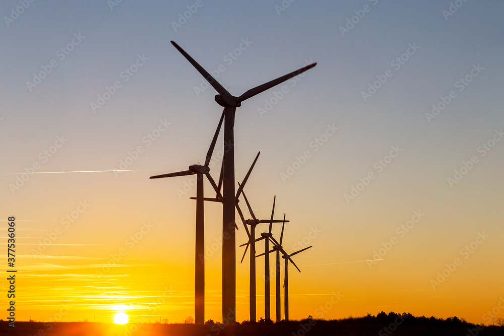 Wind Turbines at Dusk. Landscape sunset with windmills. Renewal source of electricity. Wind turbines field new technology for clean energy on mountain, sunset view with colorful twilight on sky Wind Turbines at Dusk. Landscape sunset with windmills. Renewal source of electricity. Wind turbines field new technology for clean energy on mountain, sunset view with colorful twilight on sky