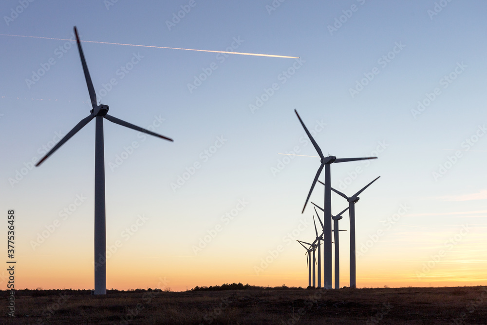 Wind Turbines at Dusk. Landscape sunset with windmills. Renewal source of electricity. Wind turbines field new technology for clean energy on mountain, sunset view with colorful twilight on sky Wind Turbines at Dusk. Landscape sunset with windmills. Renewal source of electricity. Wind turbines field new technology for clean energy on mountain, sunset view with colorful twilight on sky