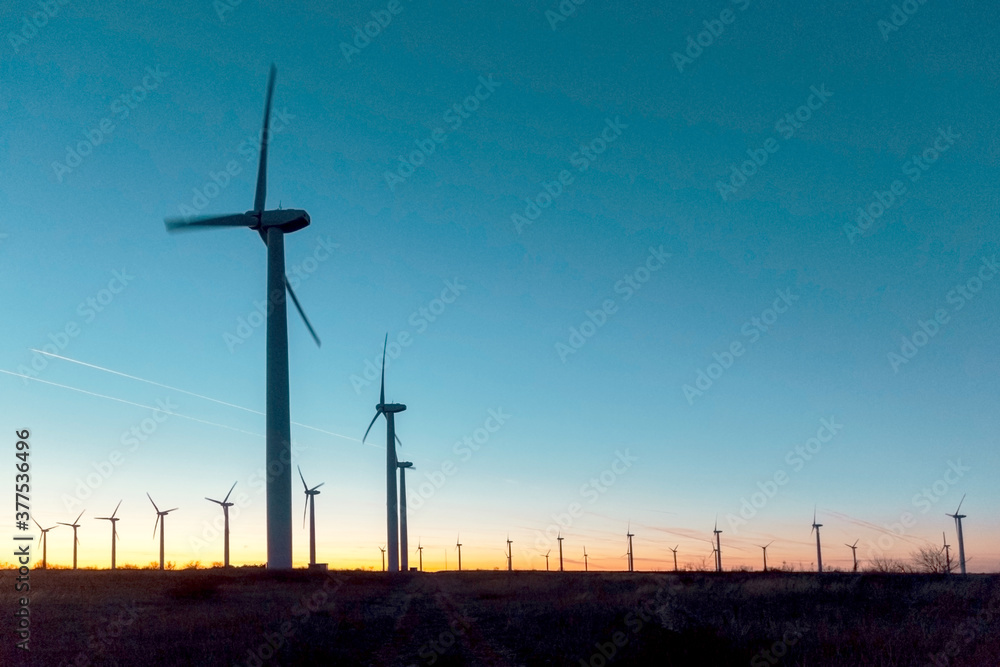 Obraz premium Wind Turbines at Dusk. Landscape sunset with windmills. Renewal source of electricity. Wind turbines field new technology for clean energy on mountain, sunset view with colorful twilight on sky