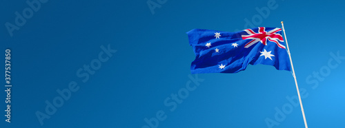 The beautiful flag of Australia waving against a blue sky in wide format. Australian national flag on background