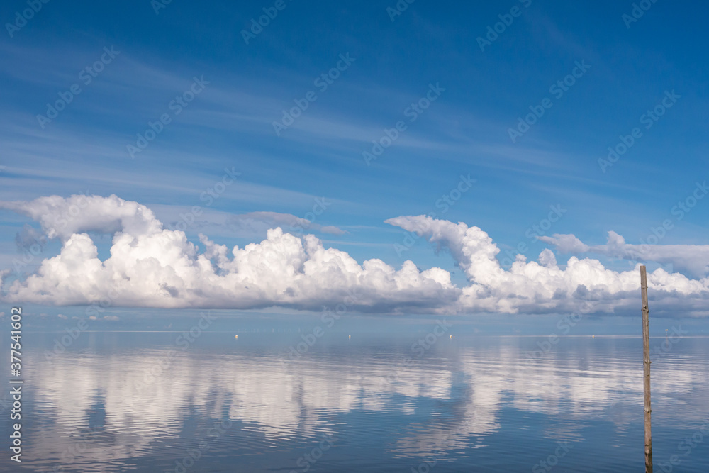 Wolkenspiegelung, bei spiegelglatter Nordsee,mit Holzpfahl,im Hintergrund Windräder.
