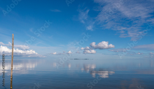 Wolkenspiegelung, bei spiegelglatter Nordsee,mit Holzpfahl,im Hintergrund Windräder.