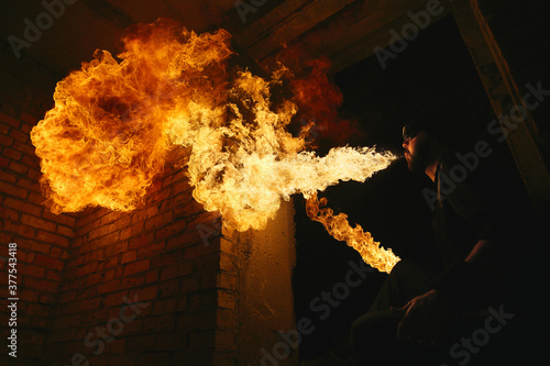Male fakir blowing out fire in an abandoned building at night. Fire performer blowing out fire close-up. © Myshkovskyi