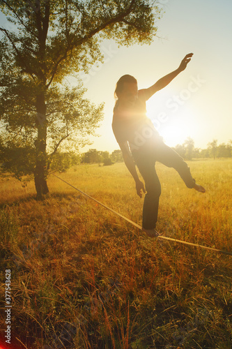  Young man walking on slackline in the meadow at sunset.
