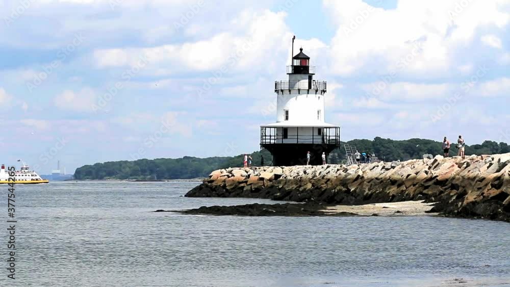 Portland Breakwater Lighthouse also know as Bug Light with a yellow ferry passing and people walking on the jetty. Portland Breakwater Lighthouse also know as Bug Light with a yellow ferry passing and people walking on the jetty.