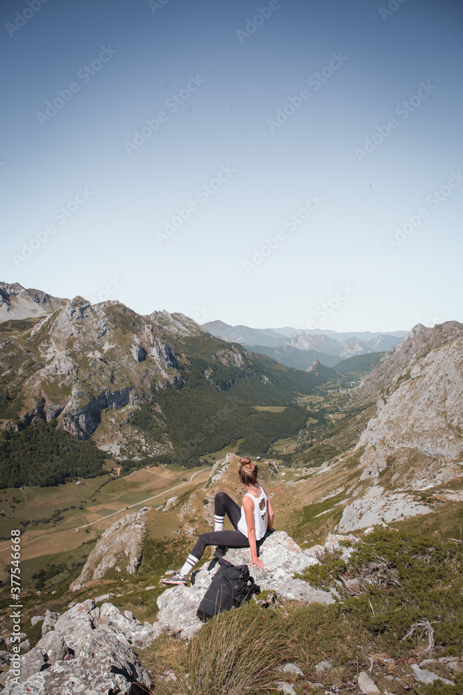 Young woman sitting on the rock watching the beautiful landscape of Somiedo natural park in Asturias, Spain, mountain valley