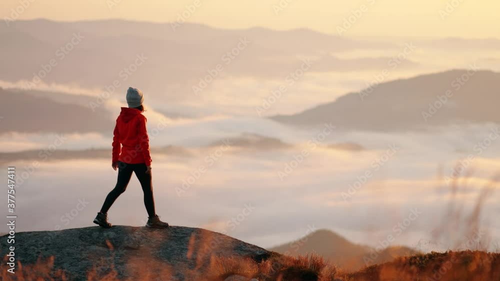 Young inspired woman standing on the top of a mountain above the clouds ...