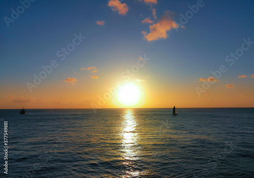 Beautiful sunset with large yellow sun above the sea surface and silhouettes of two small boats © Porthole Studio