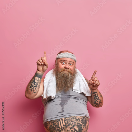 Fotografie Vertical shot of bearded Caucasian adult man gets sweaty during his training session, works hard on losing excess weight and points above