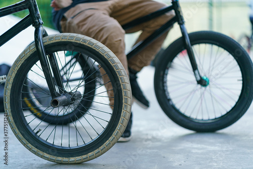 BMX in Moscow public park. Brave young biker resting after stunt in summer day. Extreme sports is very popular among youth. Side view. Defocused background.
