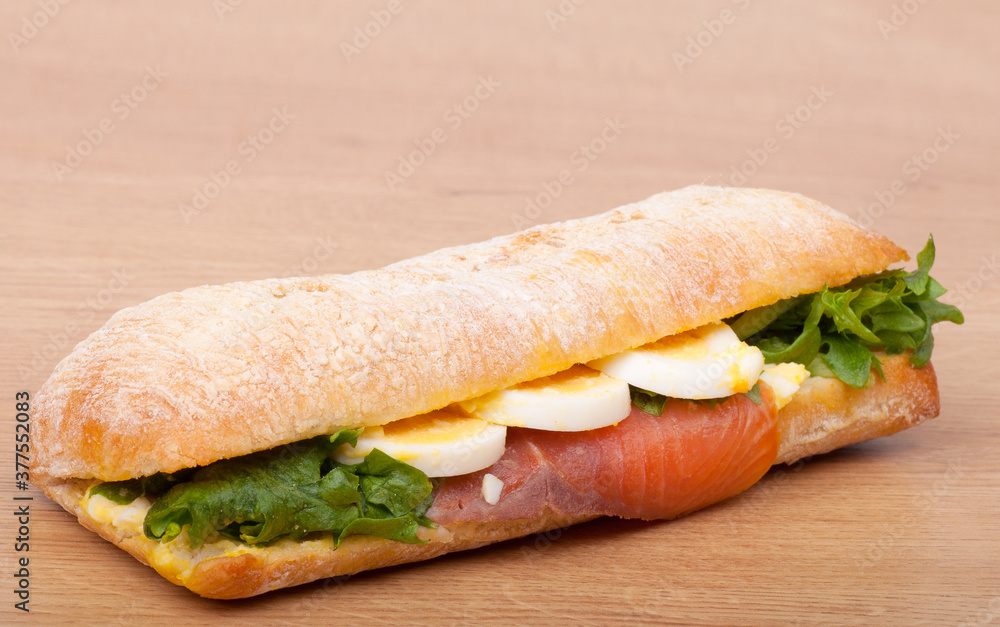 Real sandwich with smoked salmon, eggs and green on a wooden background Real sandwich with smoked salmon, eggs and green on a wooden background