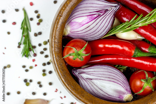 Fototapeta Naklejka Na Ścianę i Meble -  Top view of summer vegetables: onion, garlic, tomato, red chili pepper, rosemary in brown wooden bowl and peppercorns on white table background.