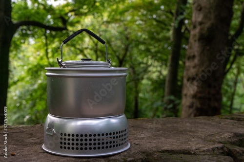 Retro camping stove with kettle resting on top of a stone wall in the forest