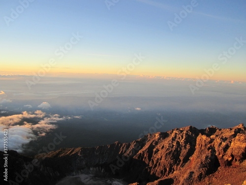 Sunrise at the top of Mount Rinjani in Lombok Island, Indonesia. View of crater lake covered in clouds from the summit. Beautiful sun rising in the horizon.