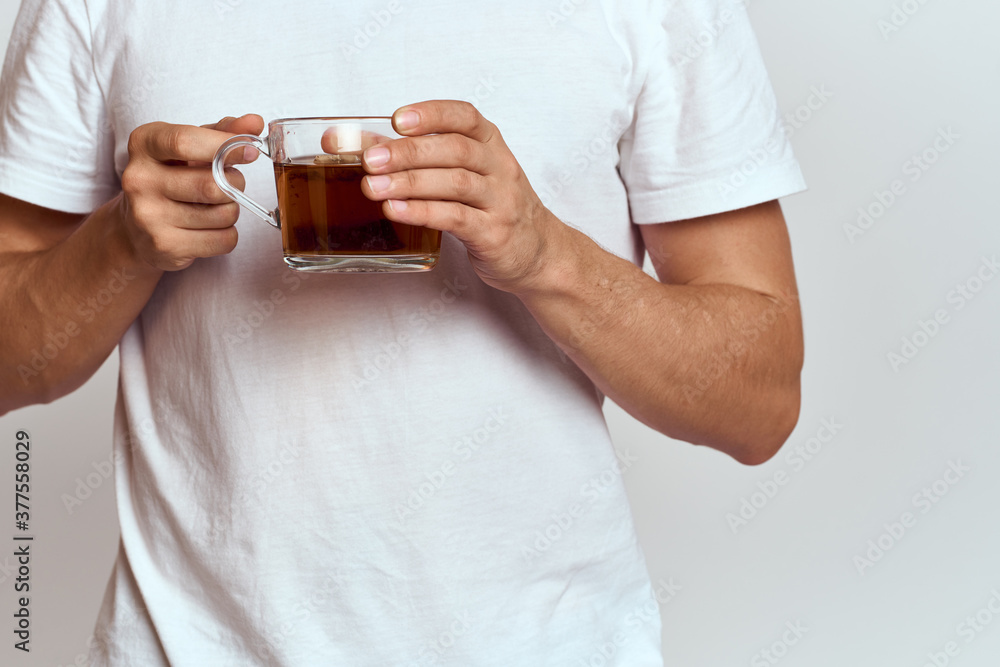 A man with a hot drink of tea in his hands in a white T-shirt on a light background cropped view A man with a hot drink of tea in his hands in a white T-shirt on a light background cropped view